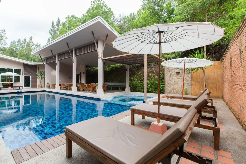 Transats et parasols ombragent une piscine rectangulaire aux carreaux bleus.