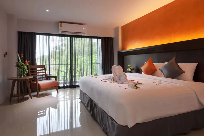 Une chambre lumineuse avec un grand lit et un fauteuil près d'une baie vitrée.