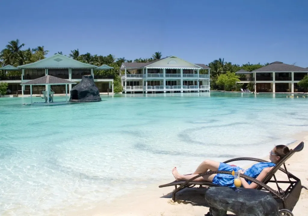 Une personne se relaxe sur une chaise longue au bord d'une étendue d'eau turquoise.