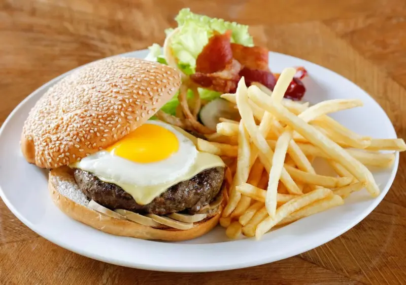 Un hamburger avec un œuf au plat et des frites est servi sur une assiette blanche.