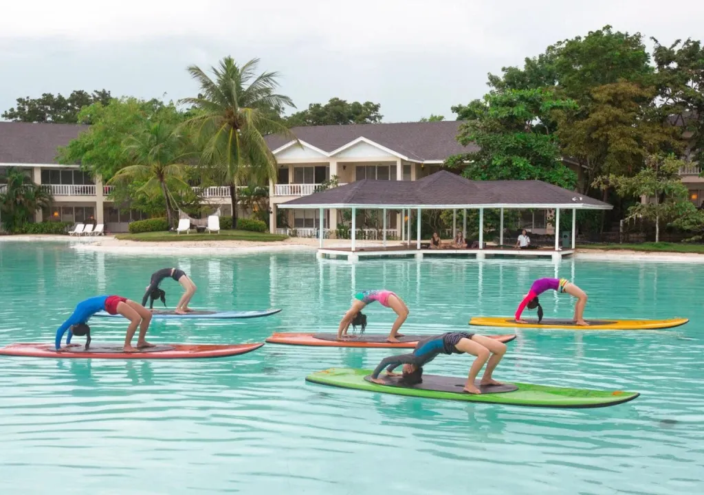 Des personnes pratiquent le yoga sur des planches de paddle dans une eau turquoise.