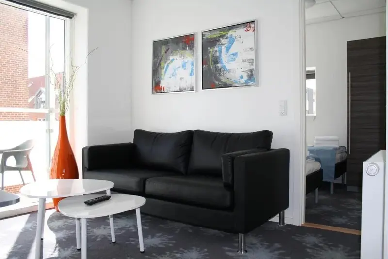 Un salon moderne avec un canapé noir et des tableaux abstraits.