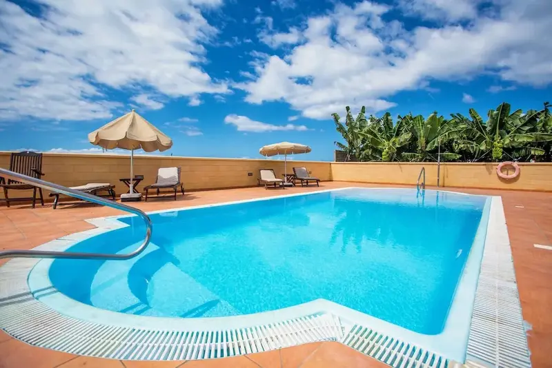 Une piscine rectangulaire avec des transats et des parasols sous un ciel bleu nuageux.
