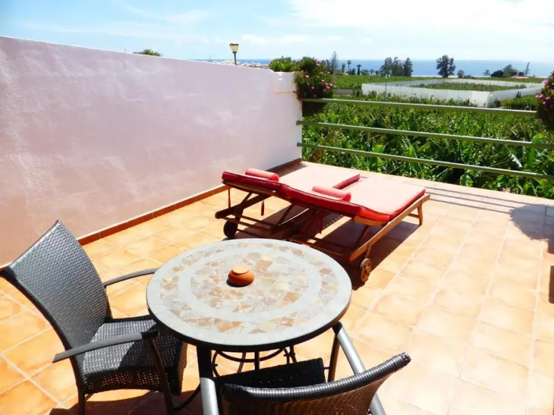 Terrasse carrelée avec mobilier de jardin et vue sur la végétation.