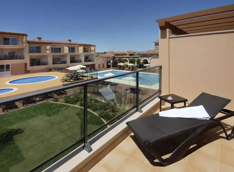 Terrasse avec transats et vue sur une piscine et des bâtiments.