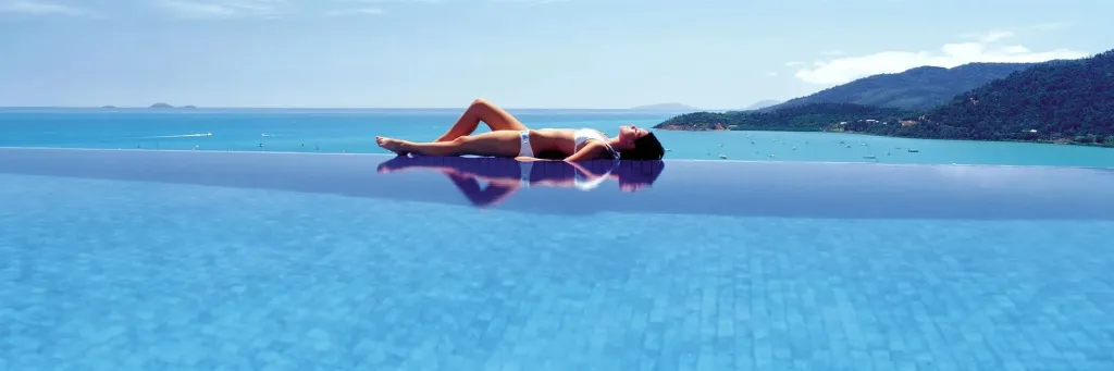 Une femme se détend au bord d'une piscine à débordement avec vue sur la mer.