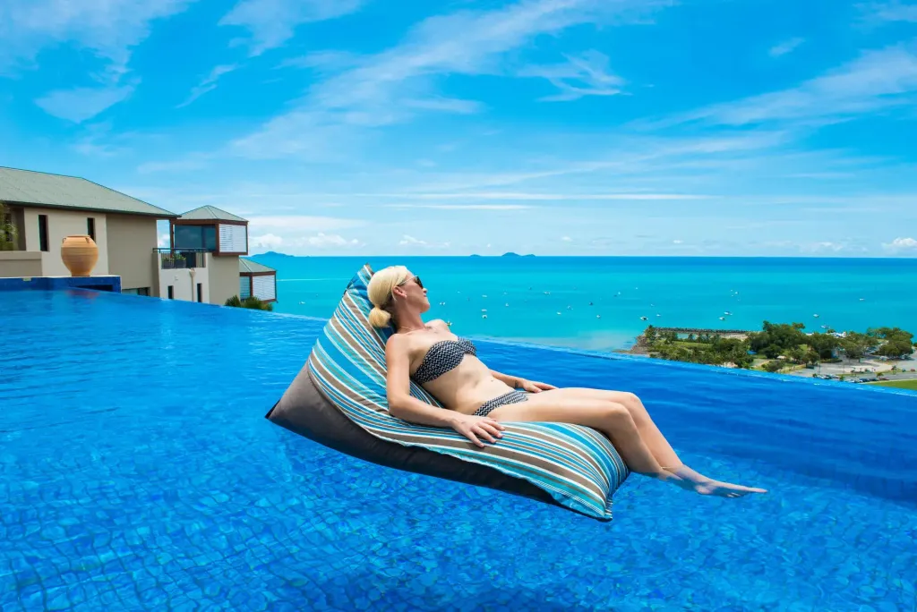 Une femme se relaxe sur un coussin flottant dans une piscine à débordement avec vue sur la mer.