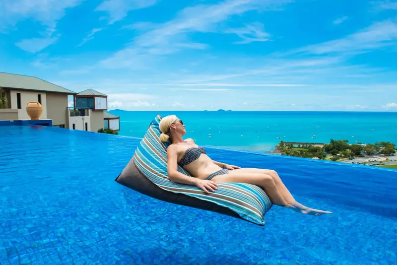 Une femme se relaxe sur un coussin flottant dans une piscine à débordement avec vue sur la mer.