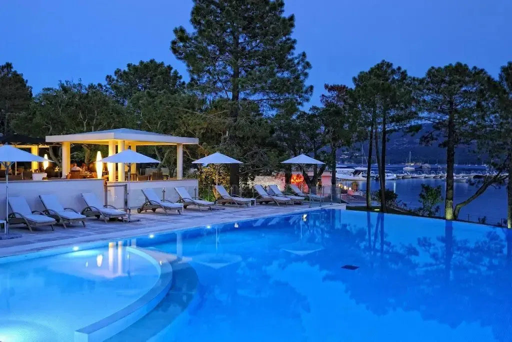 Piscine illuminée avec transats et bar en arrière-plan au crépuscule.