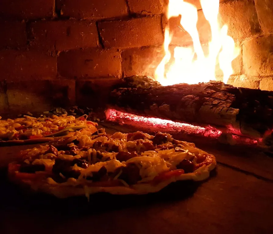 Des pizzas cuisent devant un feu de bois dans un four en briques.
