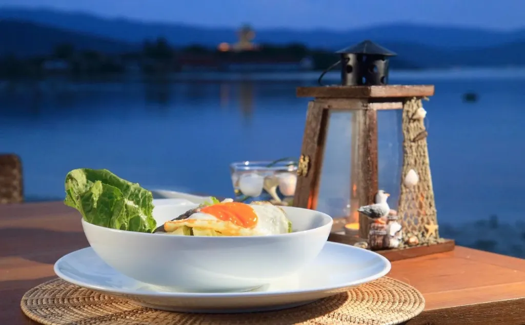 Un plat de riz et d'œuf au plat est présenté sur une table en bois face à la mer.