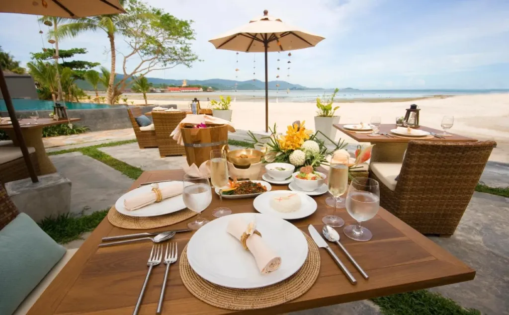 Une table est dressée avec des couverts et des plats sur une terrasse en bord de mer.