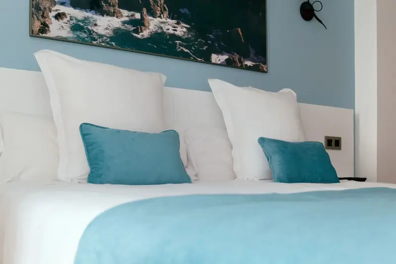 Un lit confortable avec des oreillers et une couverture turquoise est mis en valeur dans une chambre lumineuse.