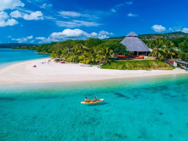 Vue aérienne d'une plage de sable blanc bordée de végétation luxuriante et d'eaux turquoise.