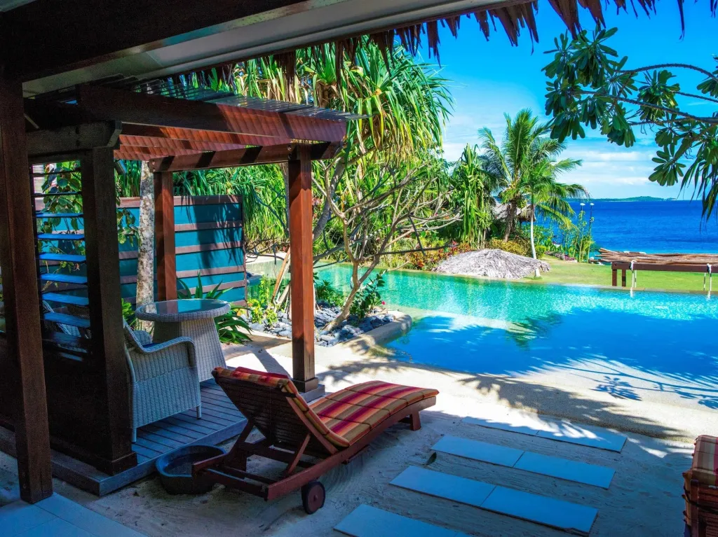 Terrasse ombragée avec transats donnant sur une piscine turquoise et la mer.