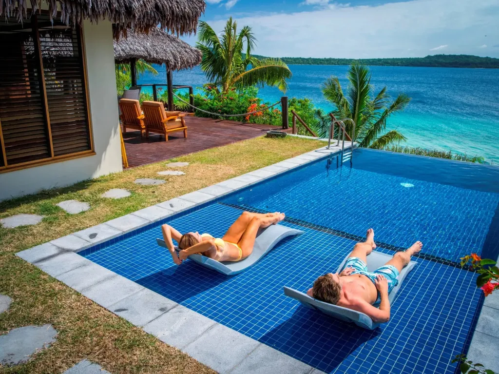 Deux personnes se relaxent sur des transats au bord d'une piscine turquoise.