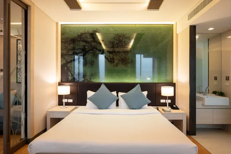 Une chambre lumineuse avec un grand lit et un décor mural végétal.