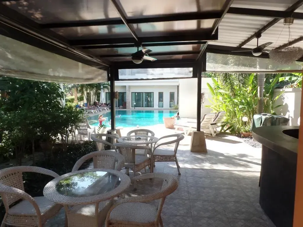 Espace extérieur ombragé avec tables et chaises donnant sur une piscine.