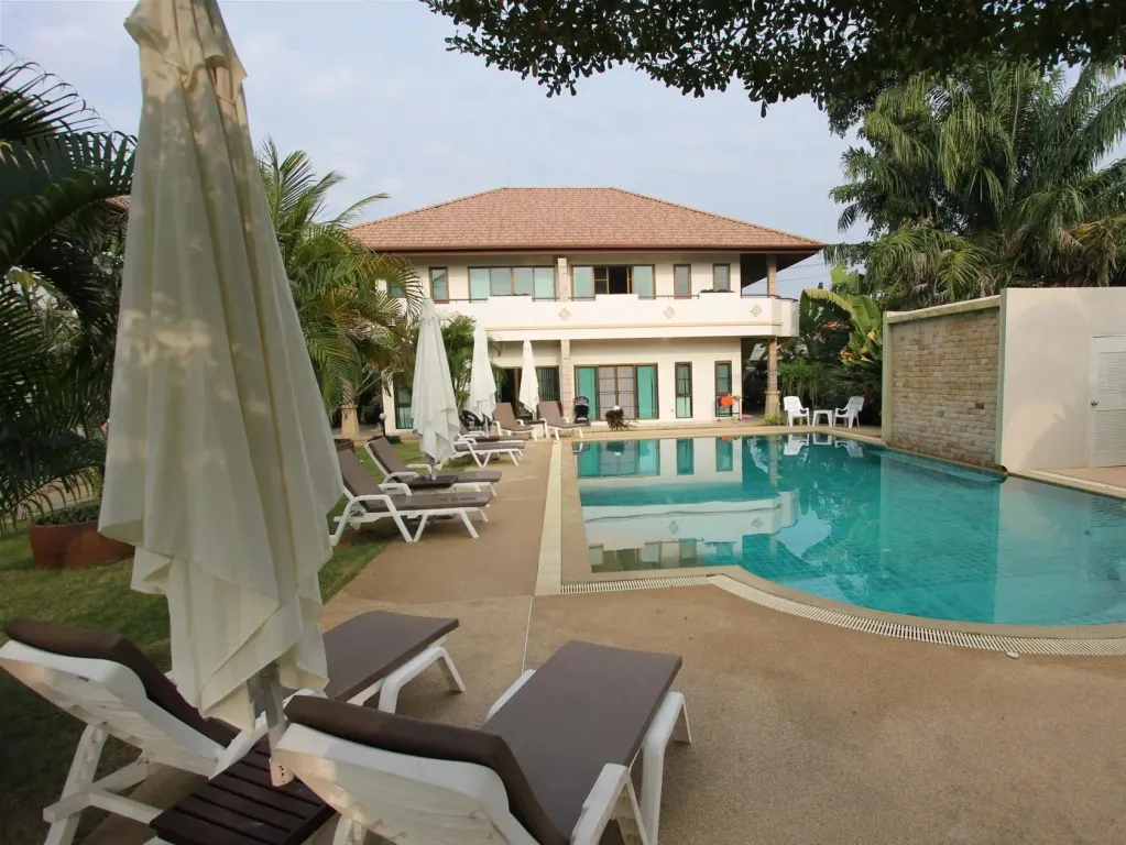 Transats et parasols bordent une piscine rectangulaire devant un bâtiment clair.