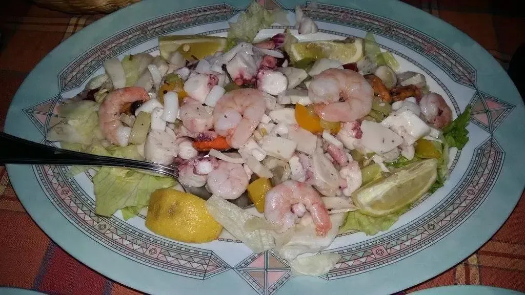 Une assiette de salade de fruits de mer est présentée avec des crevettes, du calmar et des morceaux de poisson.