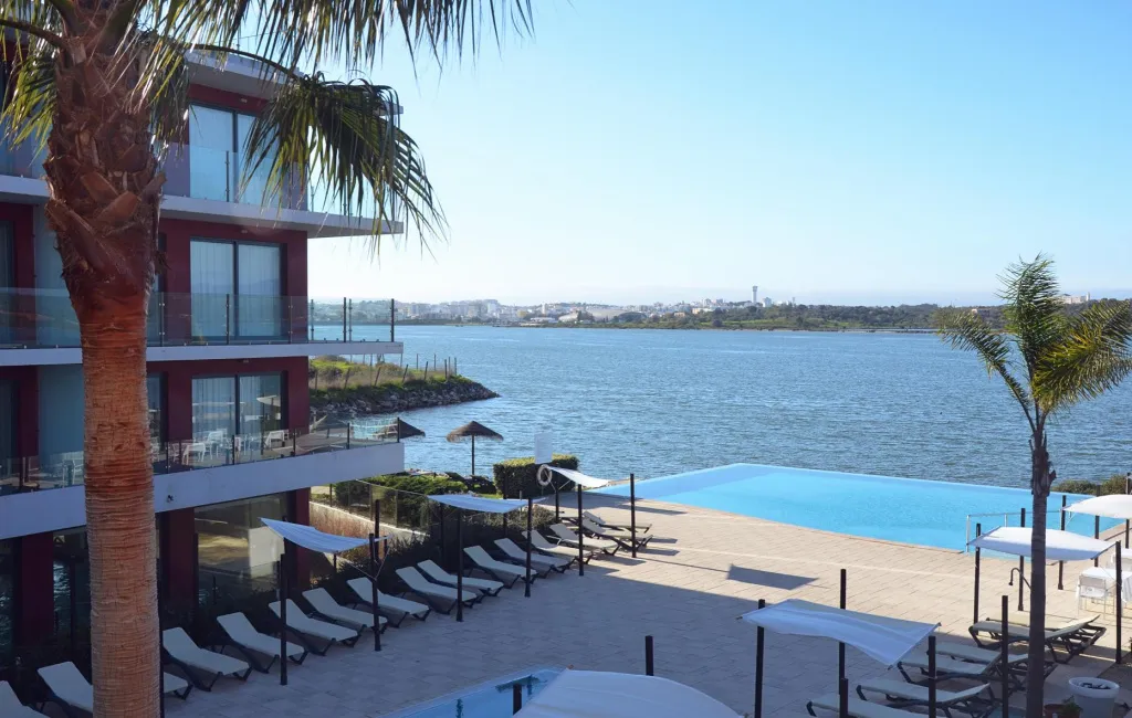 Vue d'une piscine avec transats et d'un bâtiment moderne au bord de l'eau.