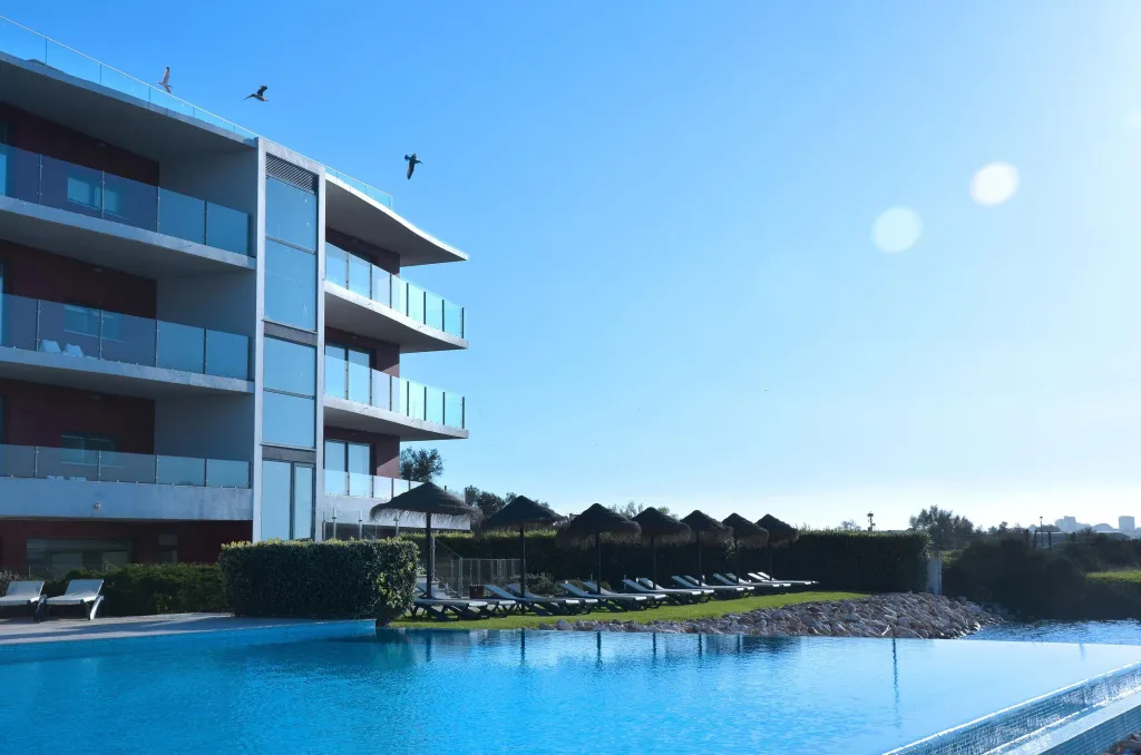 Vue d'un bâtiment moderne avec des balcons donnant sur une piscine et des parasols.