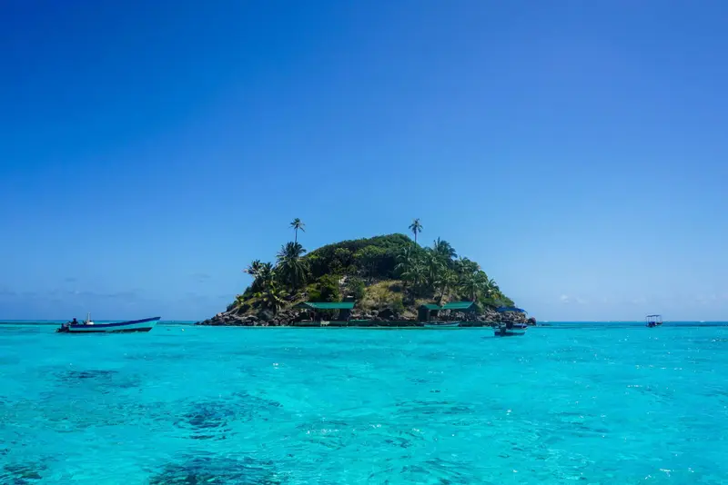 Une petite île tropicale avec des bateaux dans une eau turquoise.