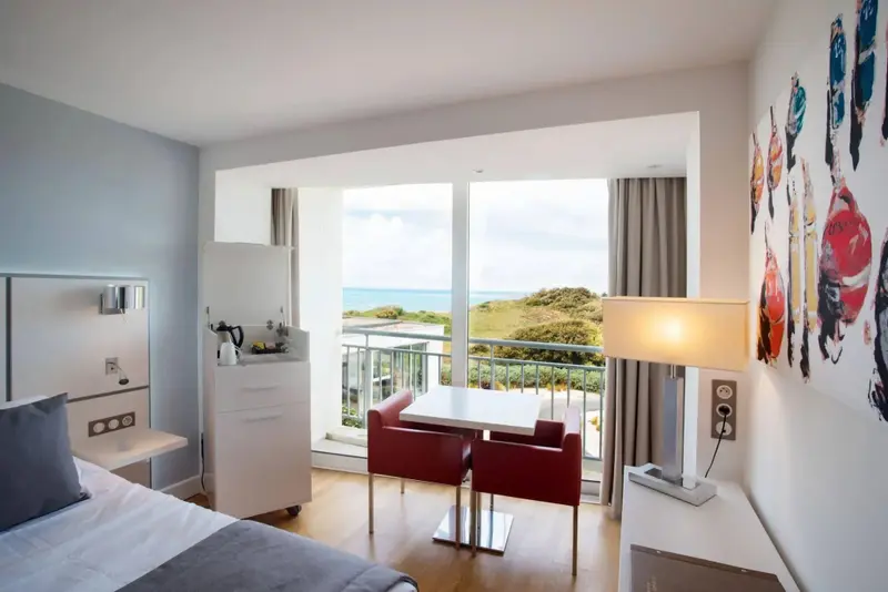 Une chambre lumineuse avec un coin repas donnant sur un paysage côtier.