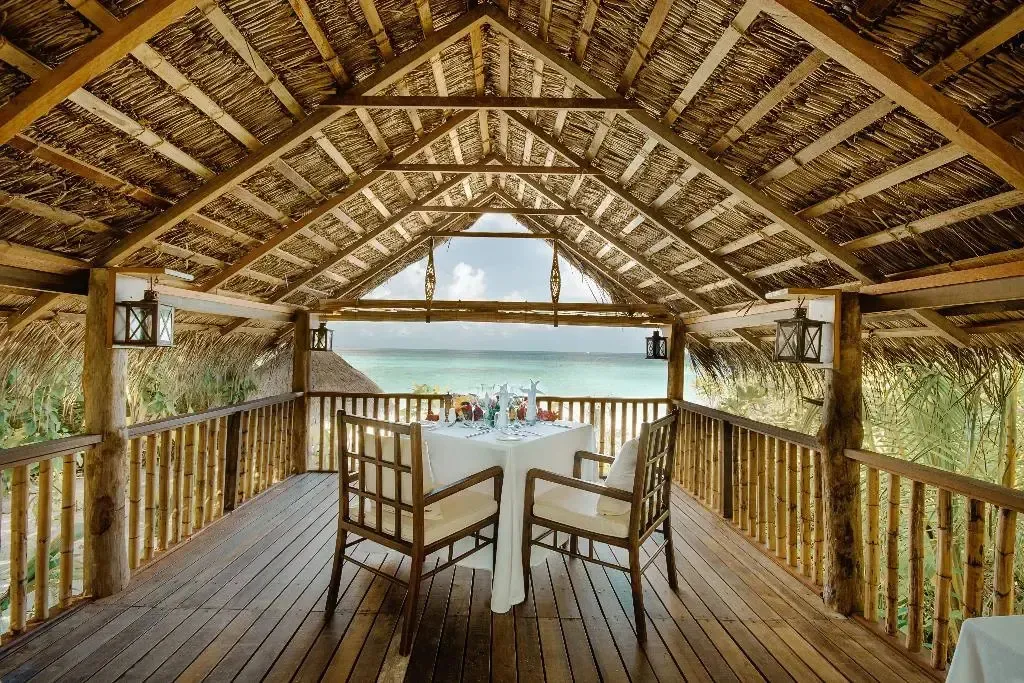 Une table est dressée sur une terrasse en bois avec vue sur la mer.