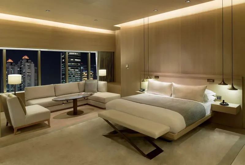 Espace de vie lumineux avec canapé et lit king-size face à une vue urbaine nocturne.