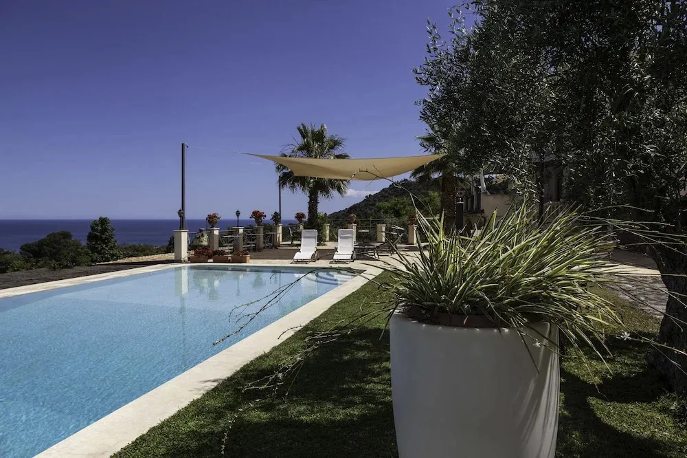 Une piscine rectangulaire bordée d'une pelouse verdoyante, avec des transats à l'ombre de voiles.