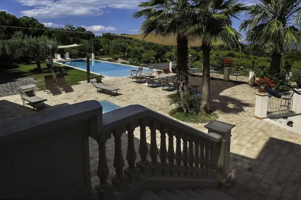 Une piscine bordée de transats et de palmiers, vue depuis un escalier.