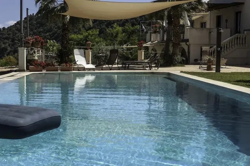 Une piscine rectangulaire avec des transats et un parasol tendu.