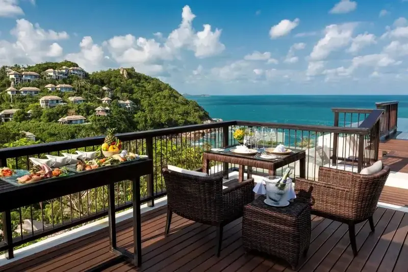 Une table est dressée pour un repas sur une terrasse en bois avec vue sur la mer.