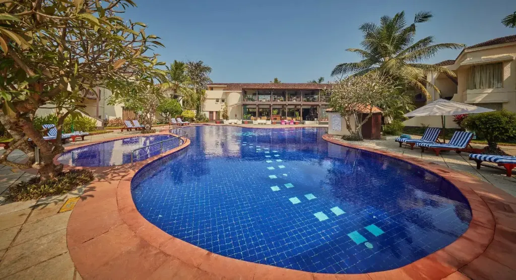 Piscine bleue entourée de chaises longues et de végétation tropicale.