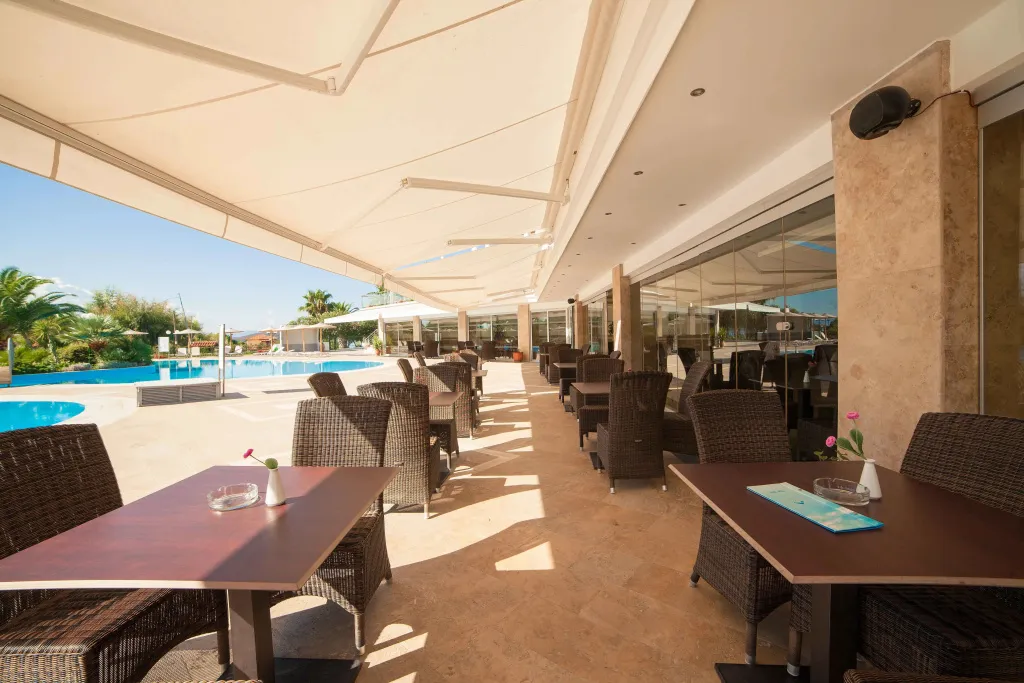 Terrasse ombragée avec tables et chaises près d'une piscine.