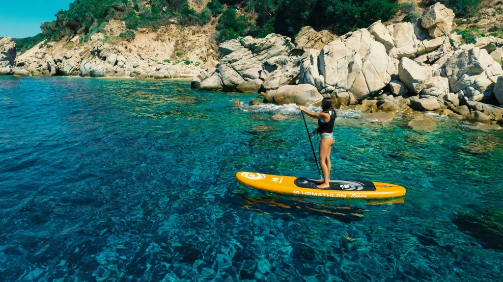 Une personne se tient debout sur une planche de paddle dans une eau turquoise.