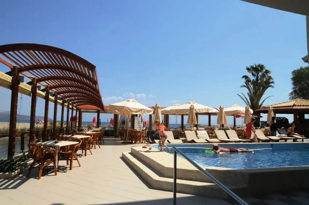 Terrasse ombragée avec tables et chaises donnant sur une piscine et la mer.