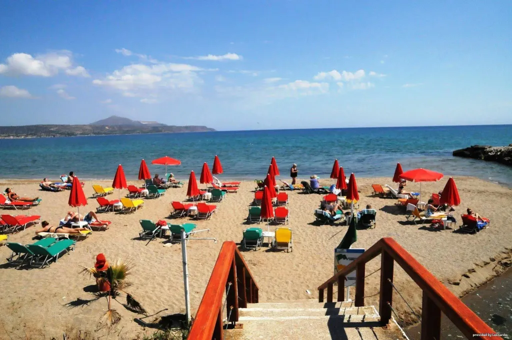 Plage ensoleillée avec transats et parasols rouges face à la mer.