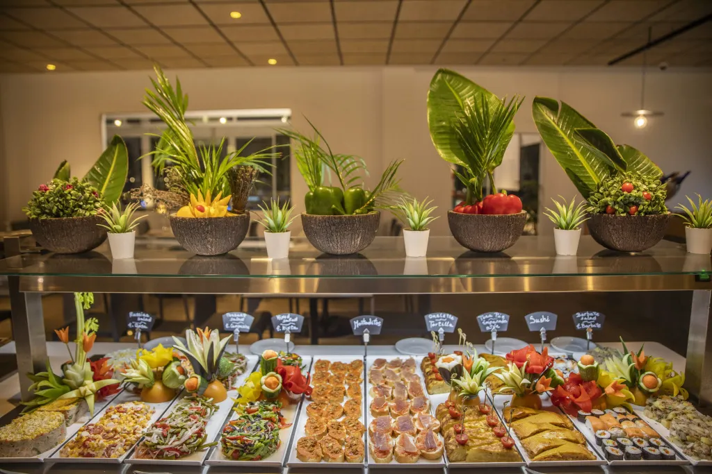 Un buffet propose une variété de plats colorés et décorés de fruits et de légumes.