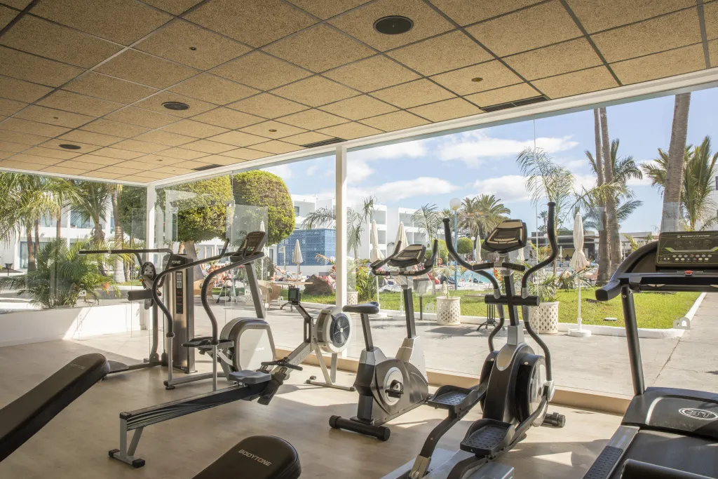 Une salle de sport lumineuse donne sur une piscine et un jardin tropical.