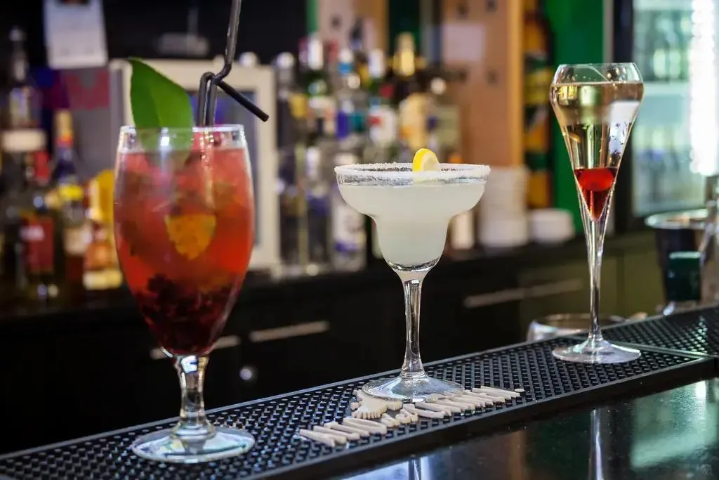 Trois verres de cocktails colorés sont alignés sur un comptoir sombre.