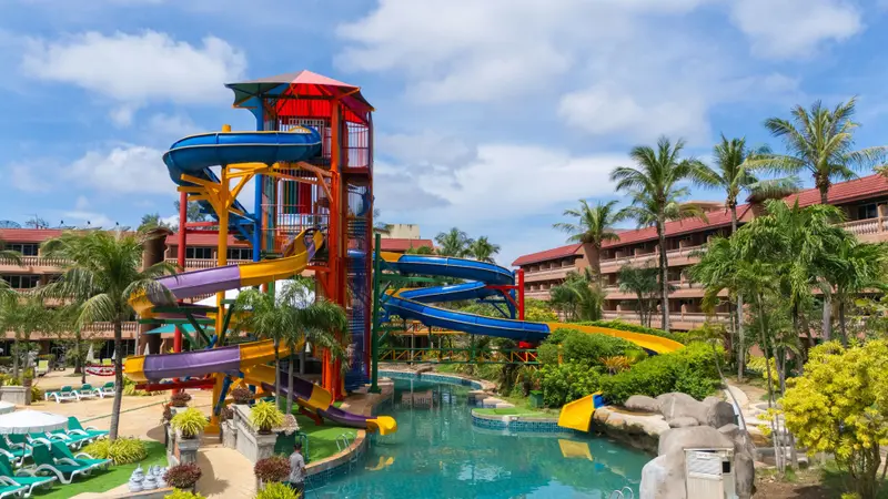 Un grand toboggan aquatique coloré domine une piscine au milieu d'une végétation luxuriante.