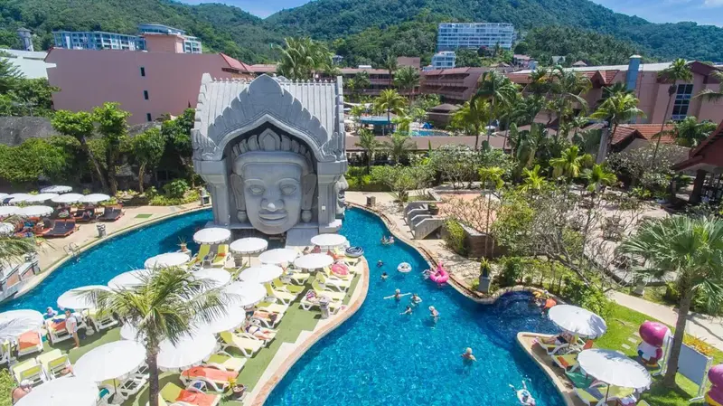 Une piscine sinueuse avec des transats et un grand visage sculpté.