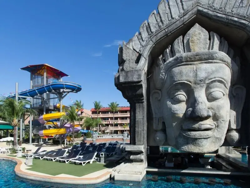 Une piscine avec une structure de toboggan colorée et une sculpture monumentale en pierre.