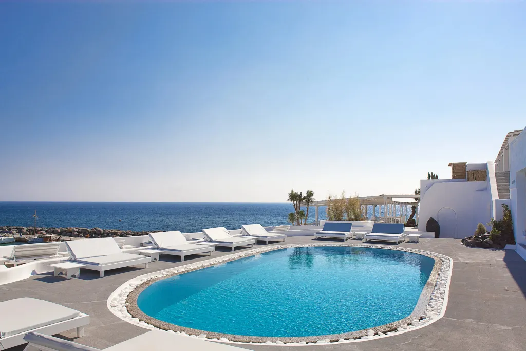 Transats blancs disposés autour d'une piscine turquoise avec vue sur la mer.
