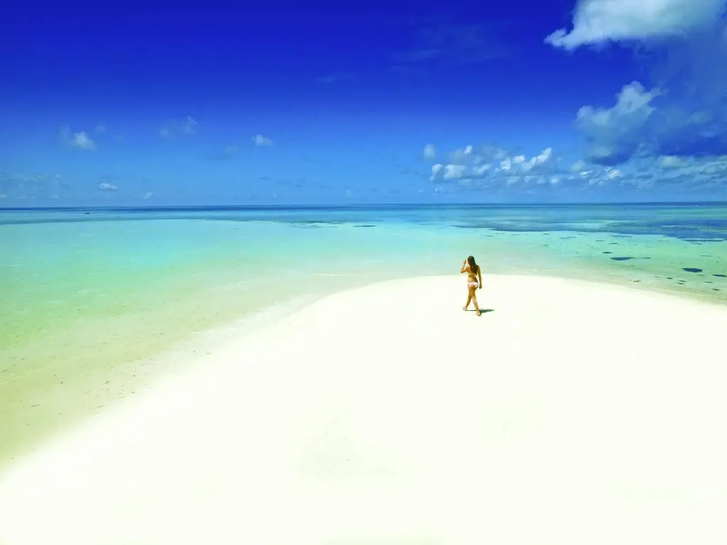 Une personne marche sur une plage de sable blanc bordée d'eau turquoise.