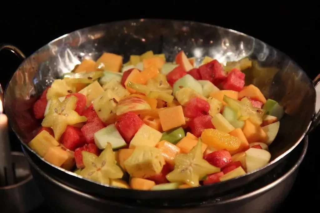 Salade de fruits frais présentée dans un grand récipient métallique.