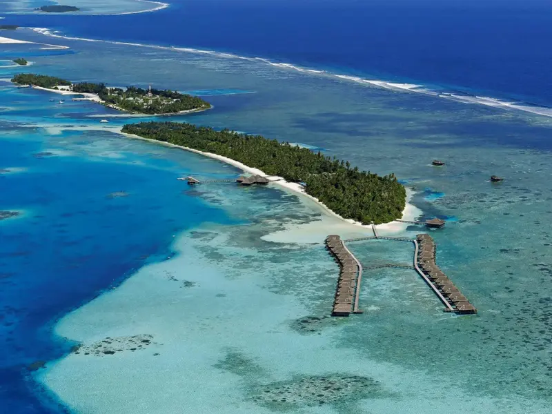 Vue aérienne d'une île tropicale avec des bungalows sur pilotis et une plage de sable blanc.