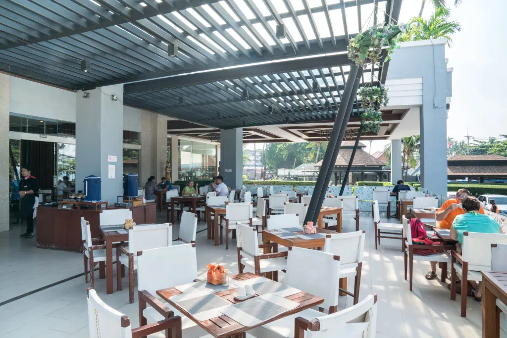 Une salle de restaurant lumineuse avec des tables et des chaises en bois et des clients attablés.